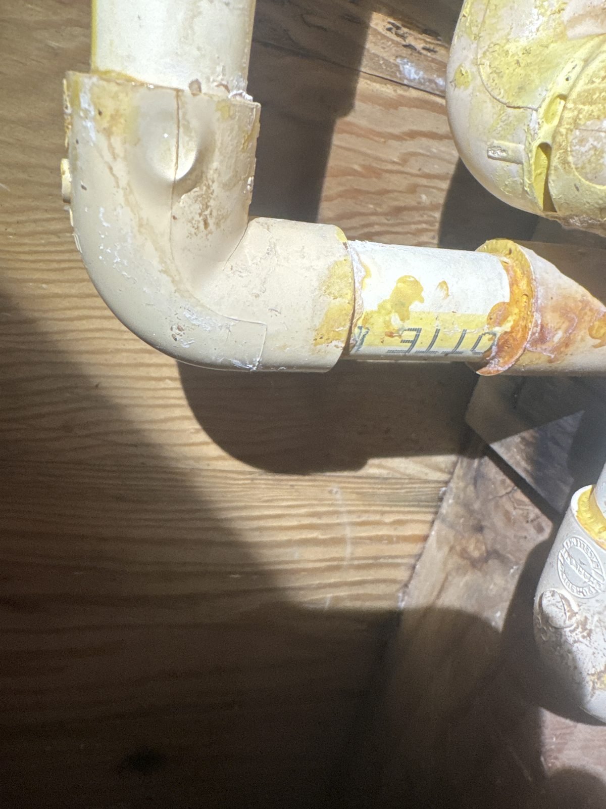 Close-up of a cracked CPVC elbow fitting with rust and mineral staining at the joint