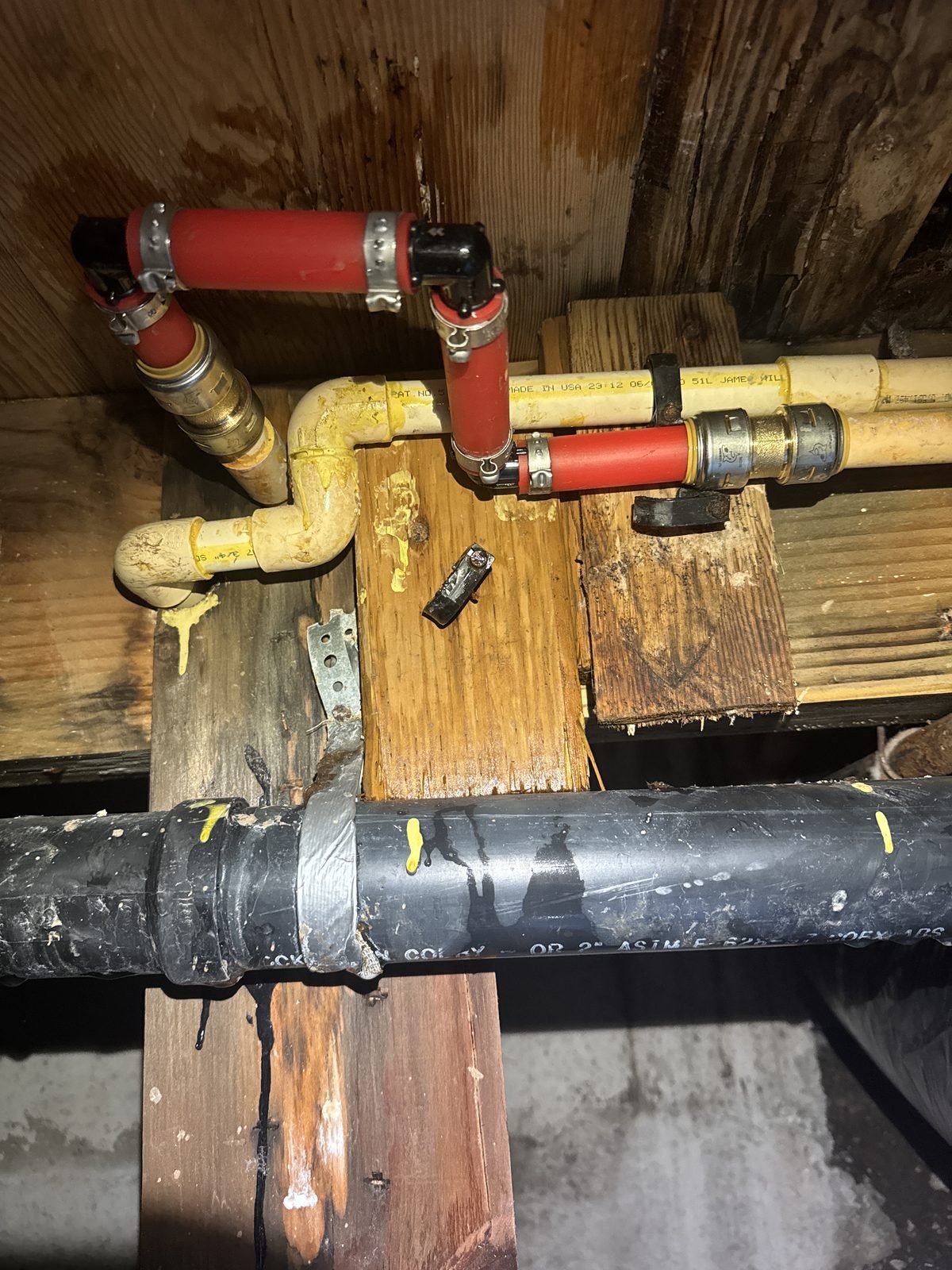 Crawlspace showing aged CPVC supply pipe patched with red PEX and brass push-to-connect fittings